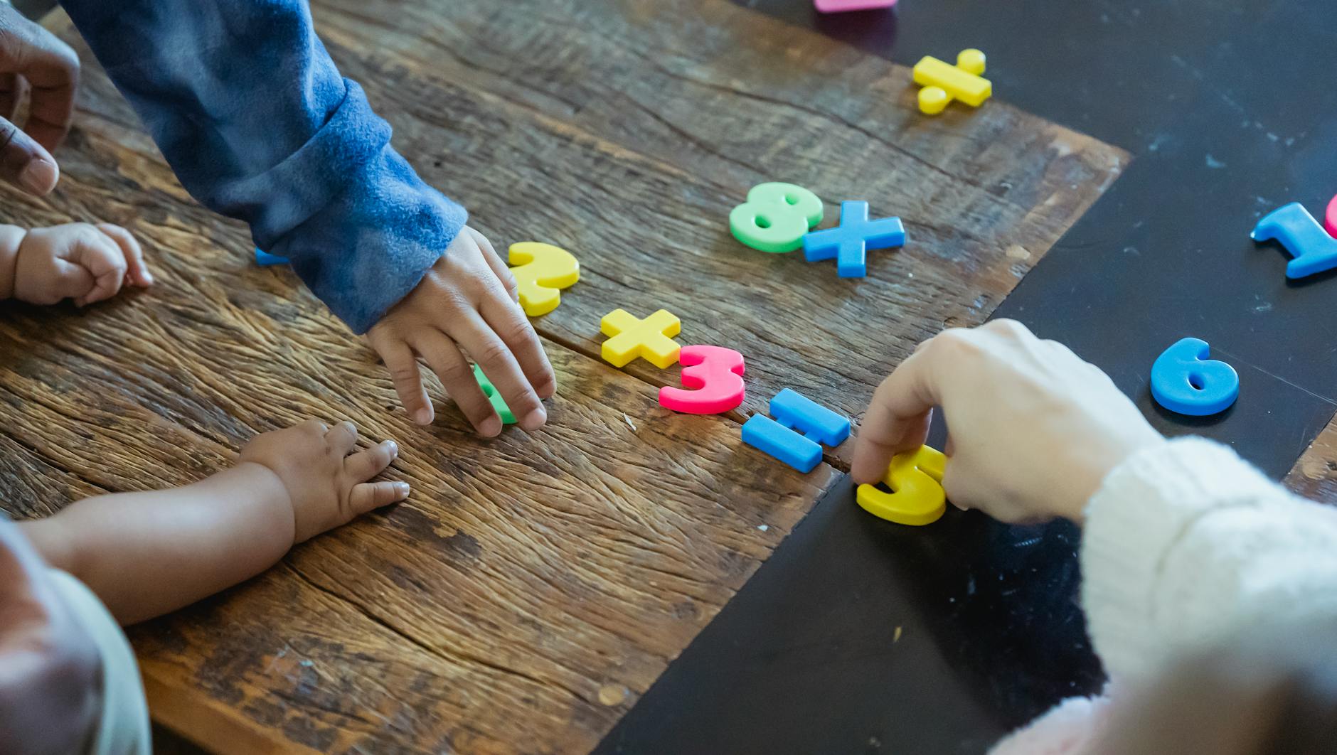 Zabawy matematyczne w przedszkolu – proste pomysły na naukę liczenia przez ruch i zabawę Dzieci bawią się kolorowymi plastikowymi cyferkami na drewnianym stole