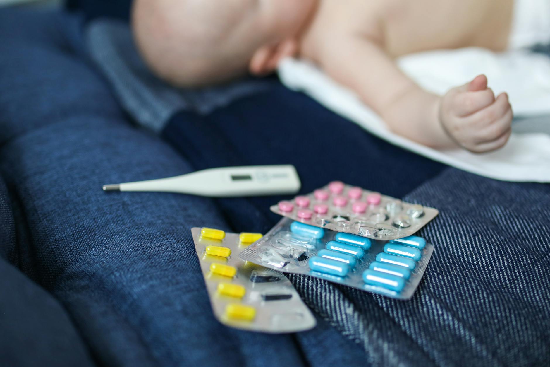 Niemowlę leży obok leków i termometru, sugerujące problemy zdrowotne