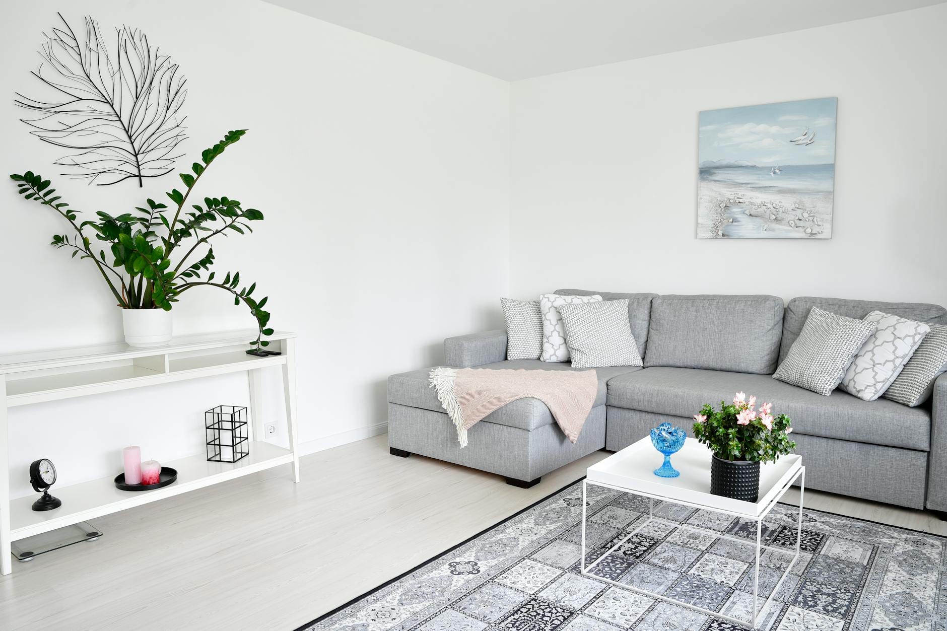 Jasny skandynawski salon z szarą sofą, roślinami i minimalistycznymi dodatkami