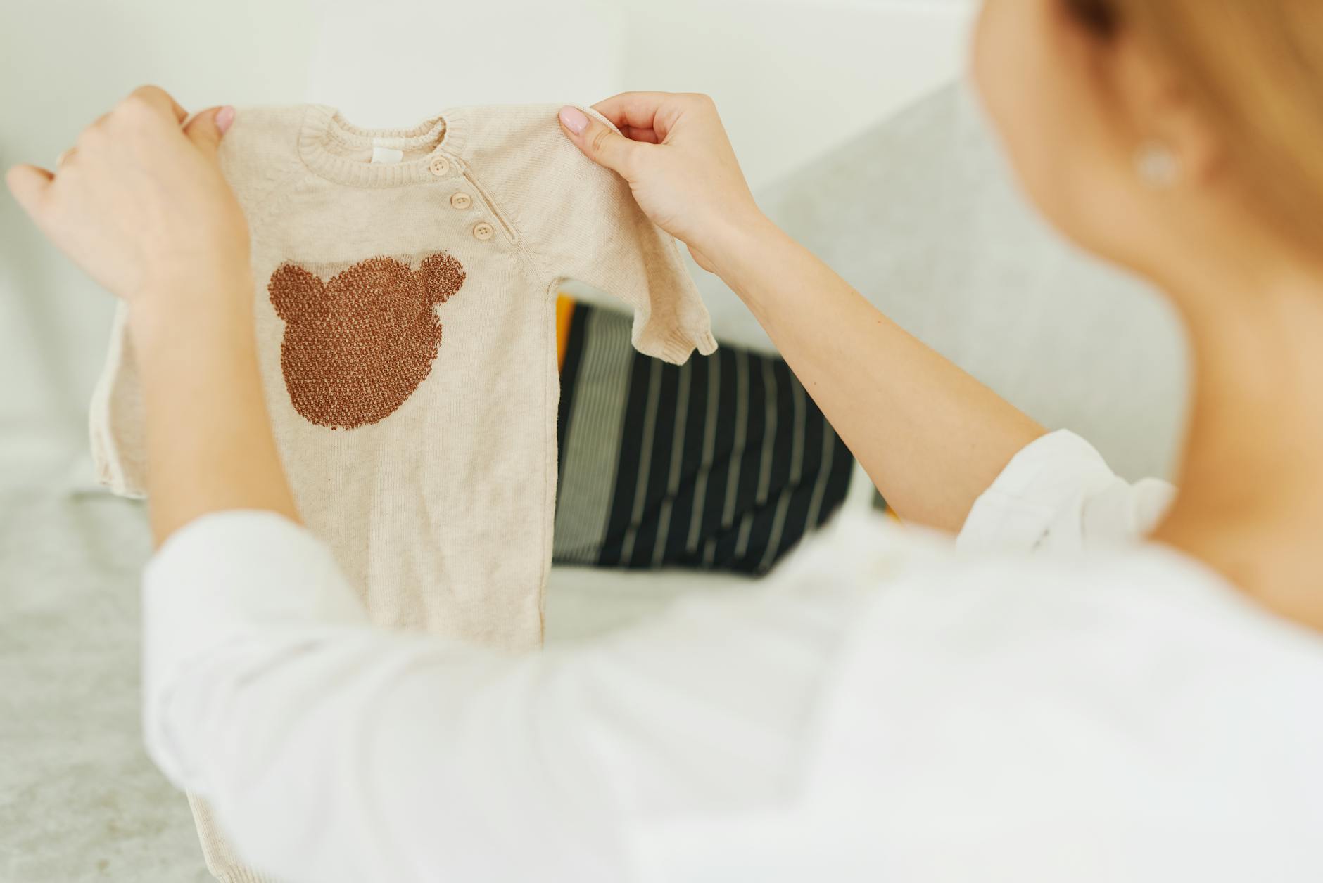 Wyprawka ubraniowa na Baby Shower: co kupić, żeby nie dublować prezentów od gości Kobieta ogląda beżowy sweterek niemowlęcy z motywem misia
