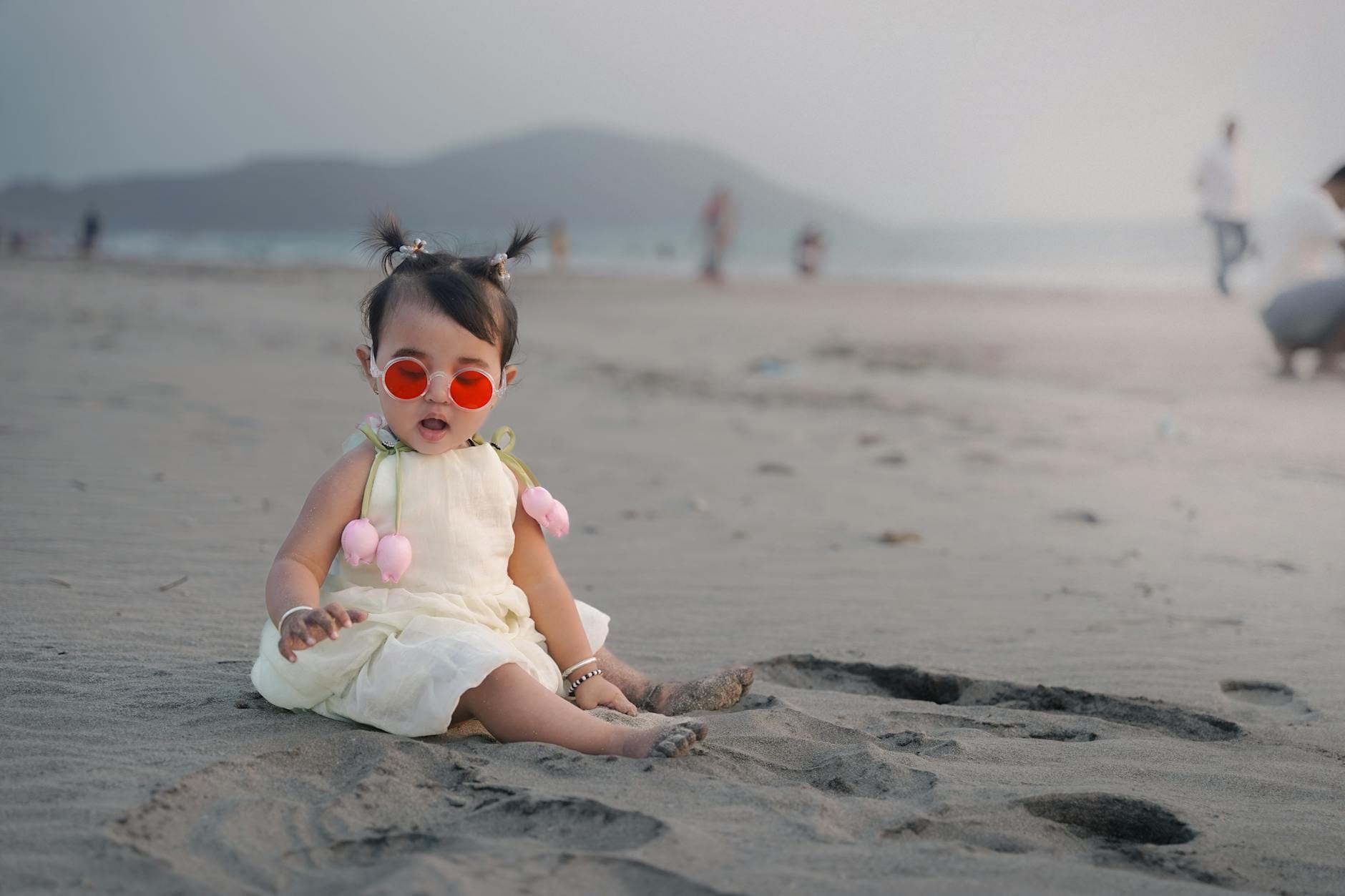 Niemowlę w okularach przeciwsłonecznych bawi się na piaszczystej plaży