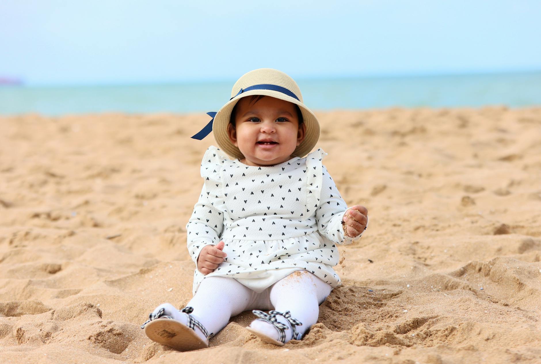 Niemowlęca dziewczynka w kapeluszu słonecznym siedzi na plaży