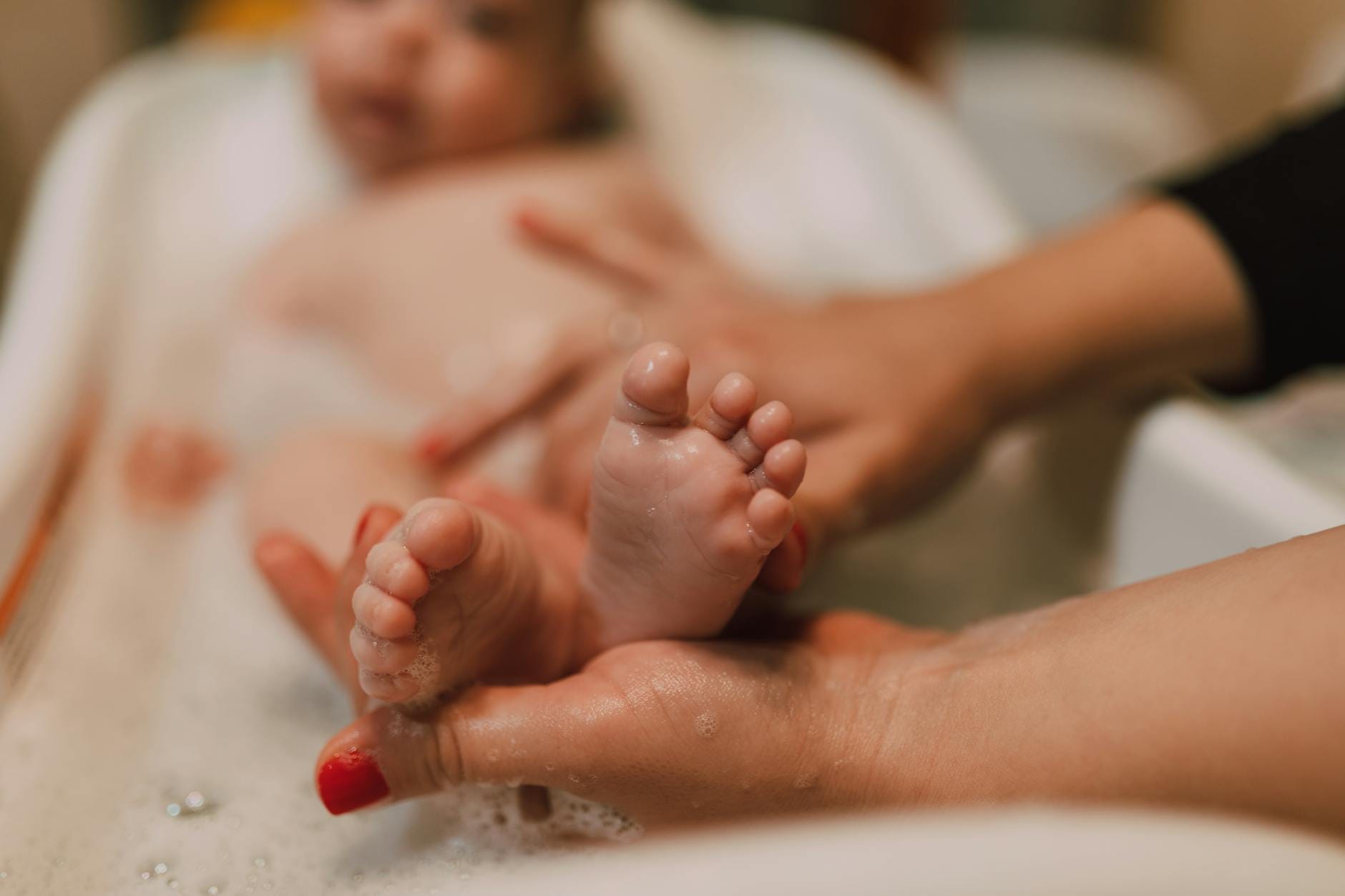 Codzienna higiena niemowlaka bez kąpieli: jak odświeżyć malucha w kilka chwil Stopy niemowlęcia w kąpieli trzymane delikatnie w dłoniach opiekuna