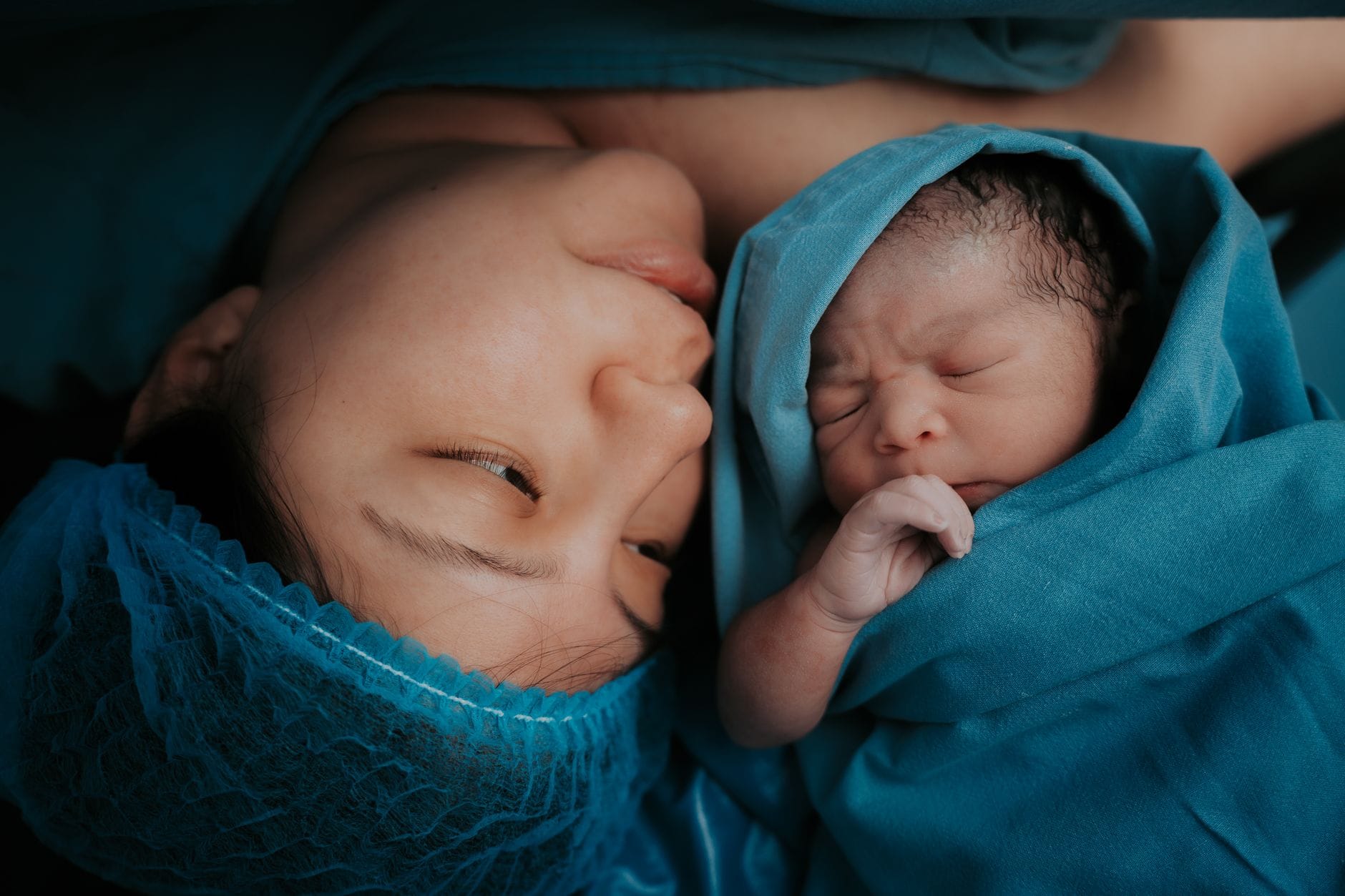 Mama przytula noworodka owiniętego w niebieski szpitalny koc