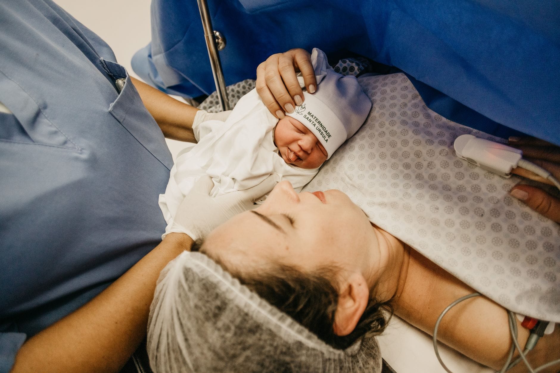 Mama tuląca noworodka tuż po porodzie na szpitalnym łóżku