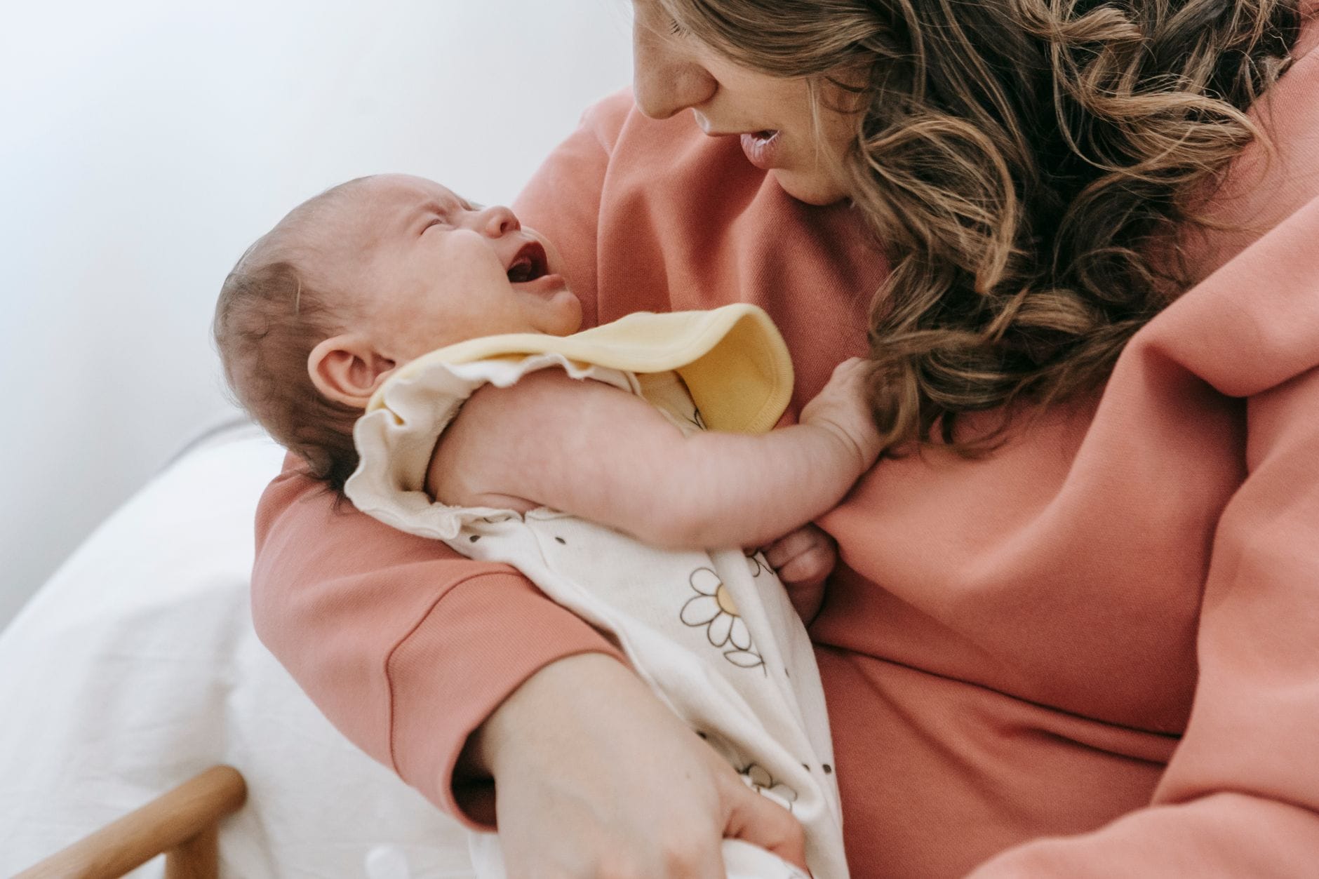 Mama tuląca płaczące niemowlę na rękach w jasnym pokoju