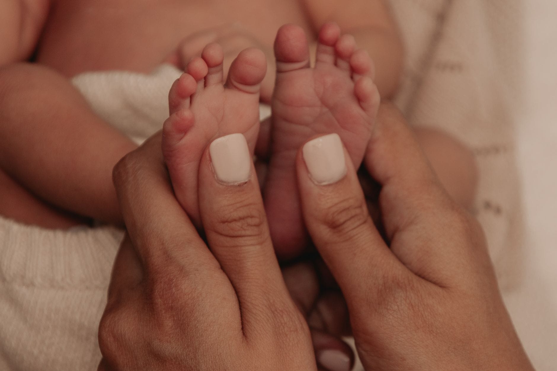 Mama delikatnie trzyma stópki noworodka podczas pielęgnacji