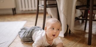 Mata piankowa czy dywan do pokoju niemowlaka? Co sprawdzi się na etapie nauki siadania Niemowlę w białym ubranku raczkujące po drewnianej podłodze